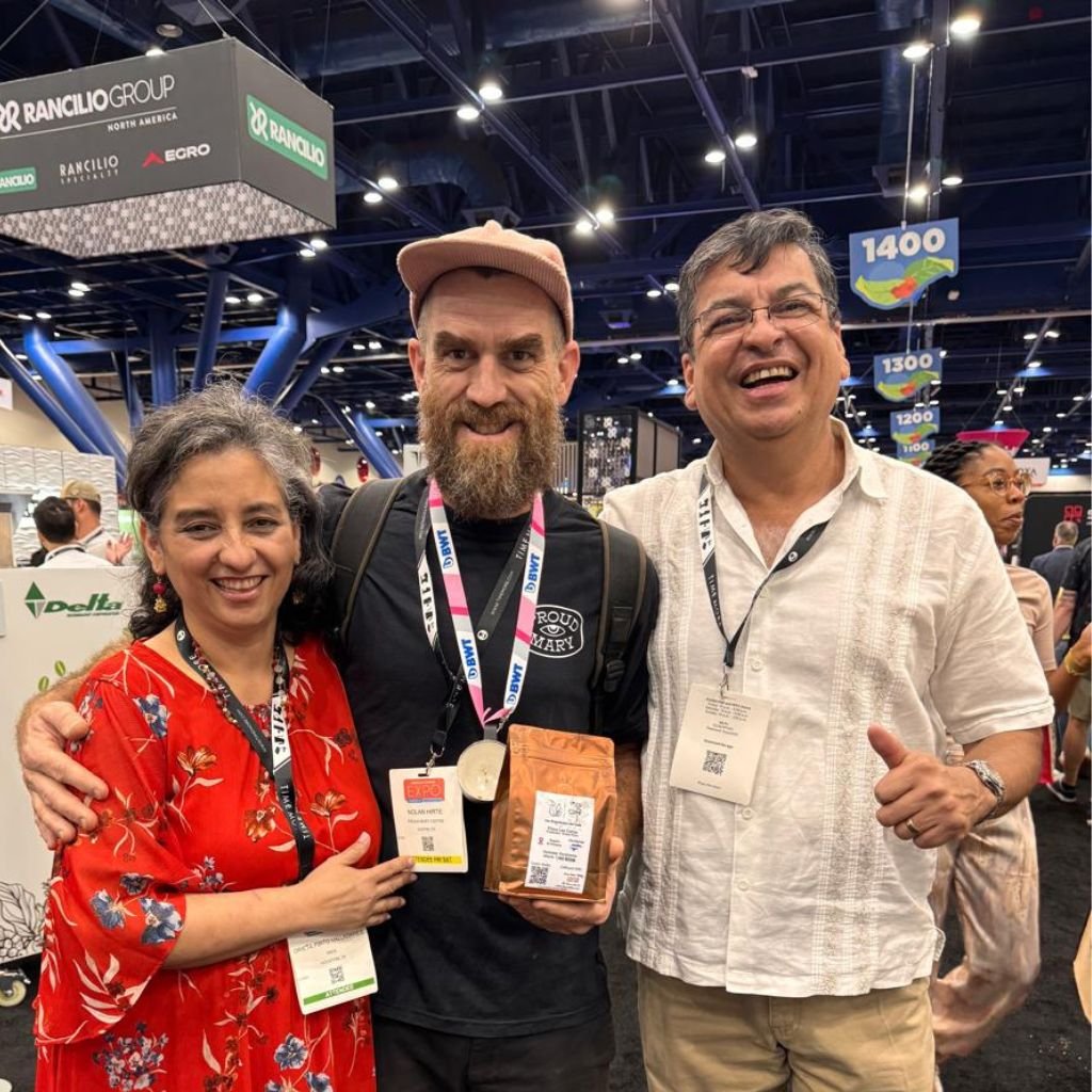 Orieta Pinto de Alvarenga y Juan Carlos Alvarenga con Mike Love (centro, con Eco Café en mano), reconocido barista y copropietario de Coffee Labs Roasters en Tarrytown, Nueva York, durante una feria internacional de café.