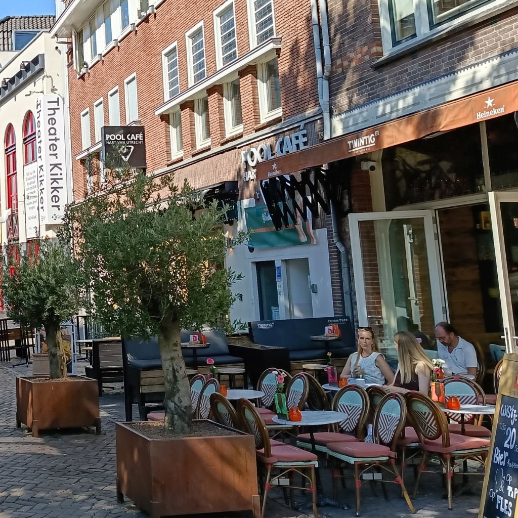 Clientes relajados en mesas exteriores de un café en una animada calle adoquinada del centro histórico de Utrecht.