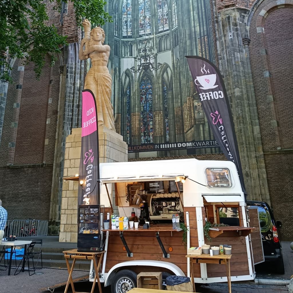 Un carrito móvil ofrece café frente a la estatua y la imponente imagen de la catedral Domkerk en Utrecht.
