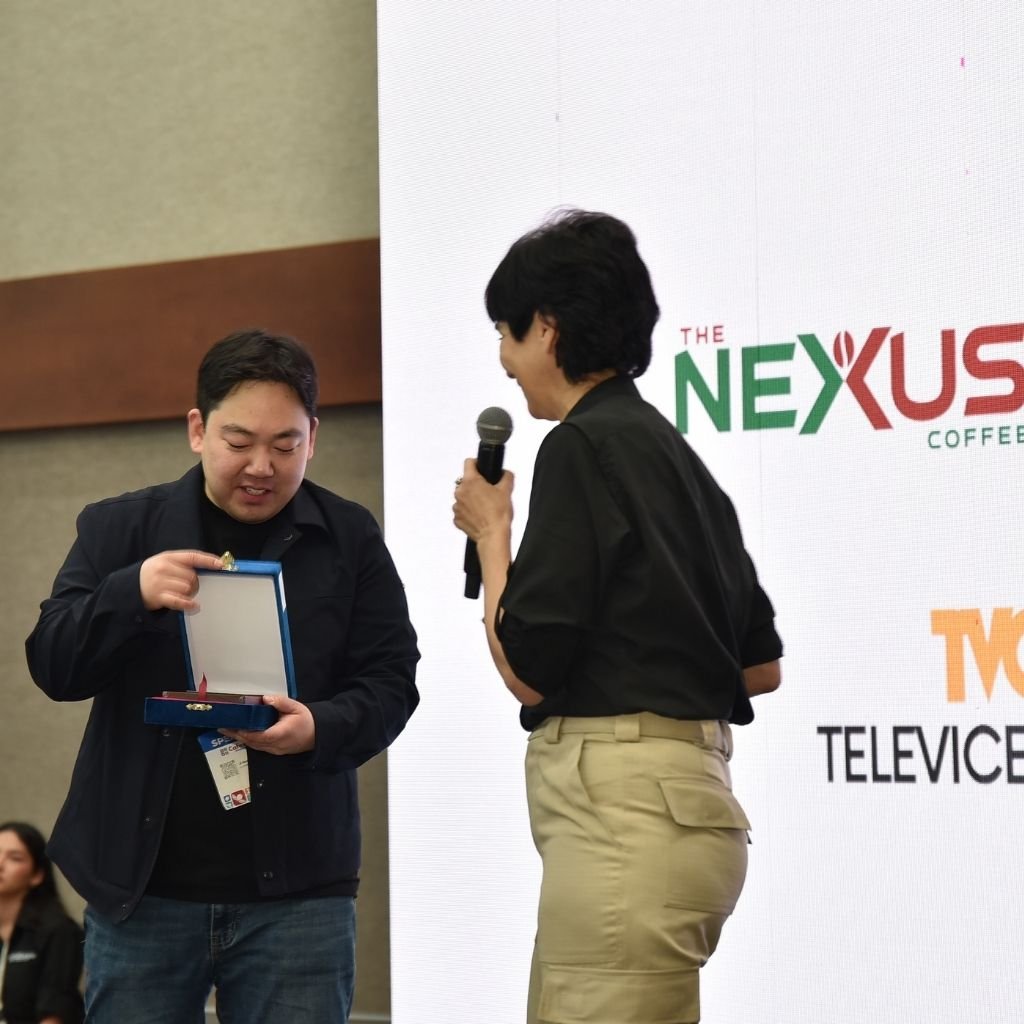 Ji Hoon Chung, fundador de Eggstone, y Karla Calidonio, de IHCAFE, entregan el premio Honduras Next Gen Auction 2025 durante CAFEXPO. The Nexus Coffee cubrió el evento como media partner